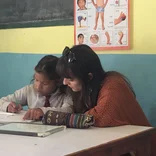 Woman helping a young girl learn in Nepal.