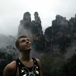 student on a hike looking up with fog and mountains behind him