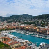 View of the port in Nice with hilly terrain peppered with buildings and trees behind it