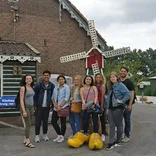 group of students standing in front of a tiny red windmill and in front of large yellow Dutch clogs