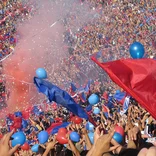 fútbol stadium filled with people wearing red and blue and holding flags
