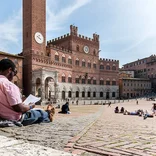 student leaning against a wall, reading in a plaza in Siena