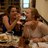 one student feeding a forkful of pasta to another student inside a restaurant in Tuscany