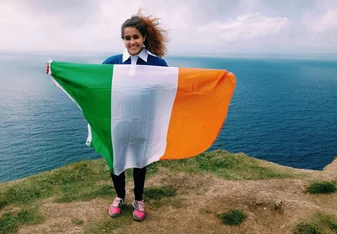 A student poses on a cliff with the Irish flag