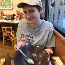 The image is a vertical picture of a girl holding a large bowl for the camera to see, which is empty. She smirks at the camera, implying she has finished the contents of the bowl.