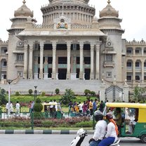 Government building in Bangalore with Indian flag flying. Two people on a moped are stopped to admire the building.