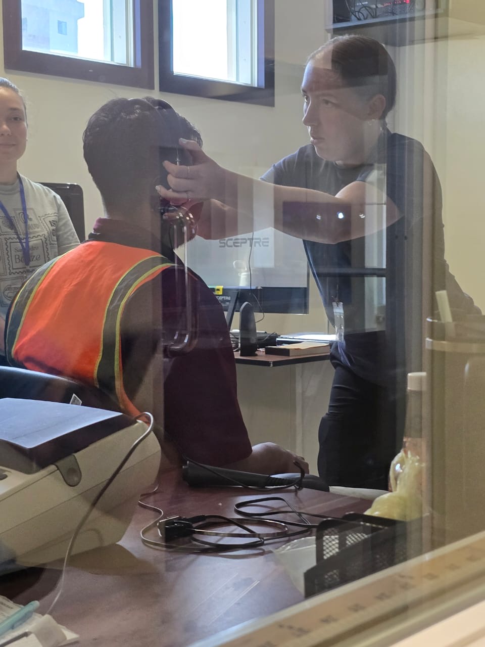 A woman is putting headphones on an airport worker in order to perform a hearing test. 
