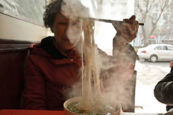 elderly woman eating noodles with a chopstick