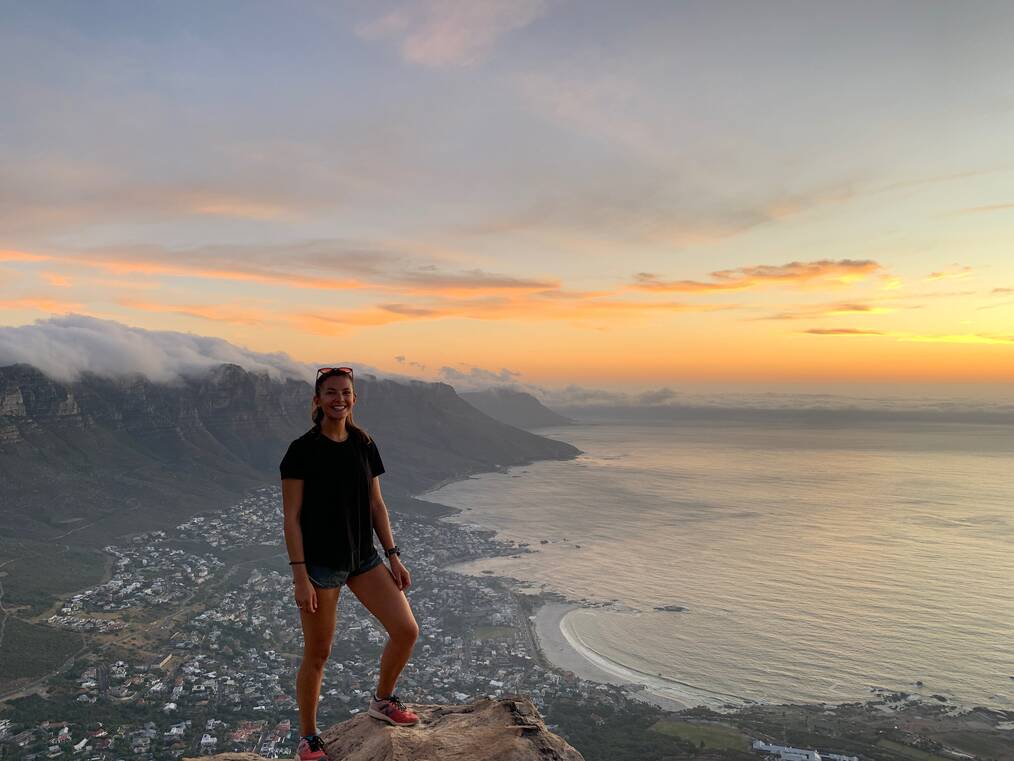 Woman standing at the edge of a cliff with a beach in the background.