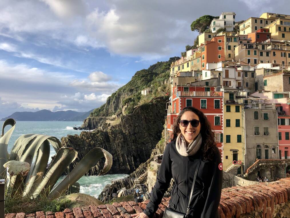 Woman sitting on wall with cliffs and buildings behind her.