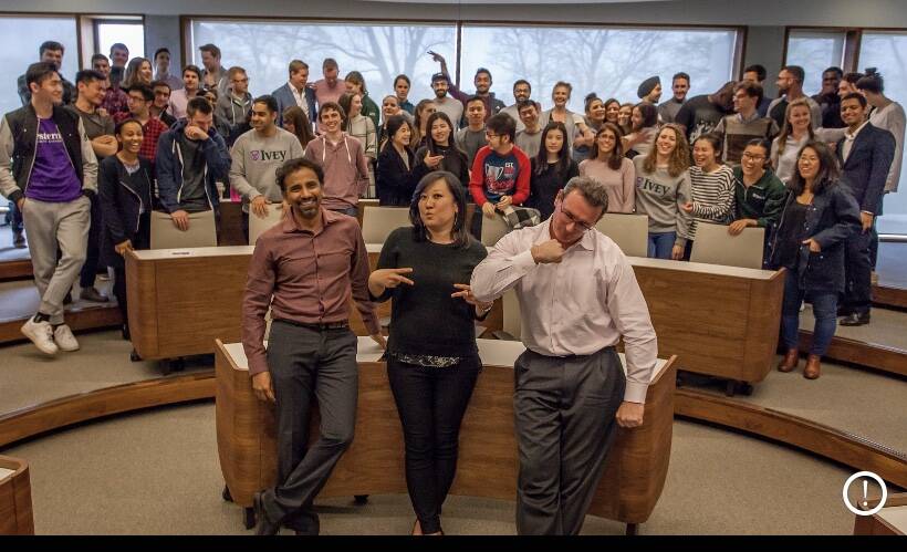 Three professors in a room full of students.