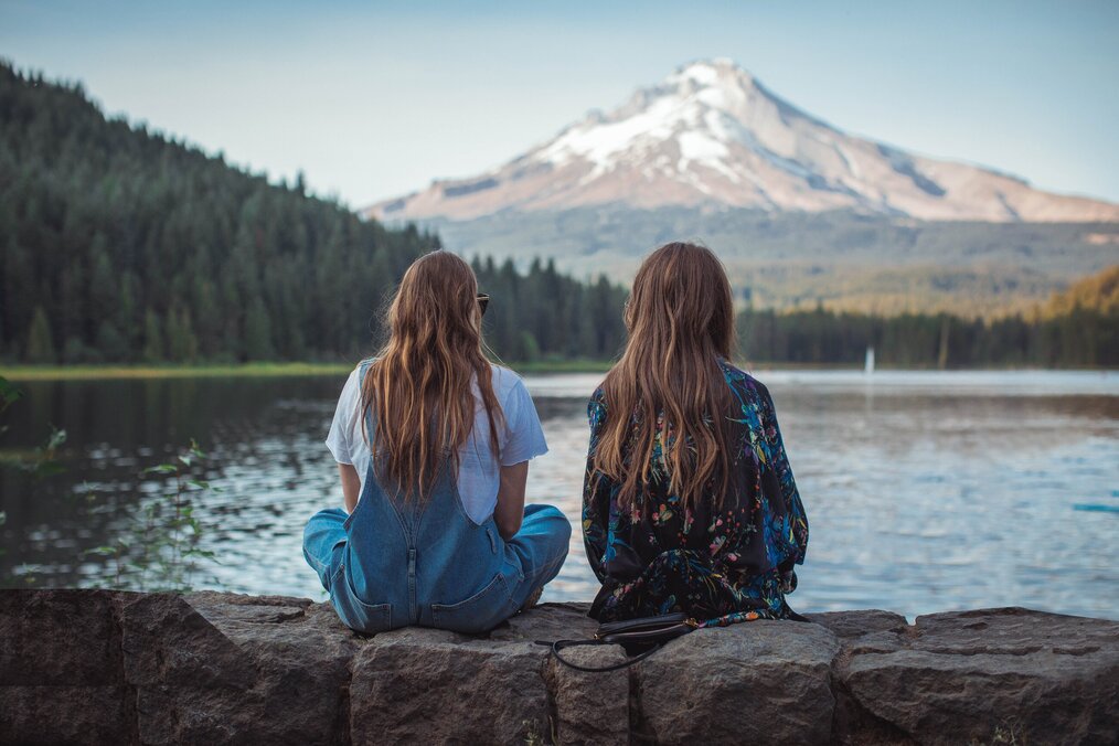 Photo by Roberto Nickson on Unsplash Two women sitting on a wall near a lake.