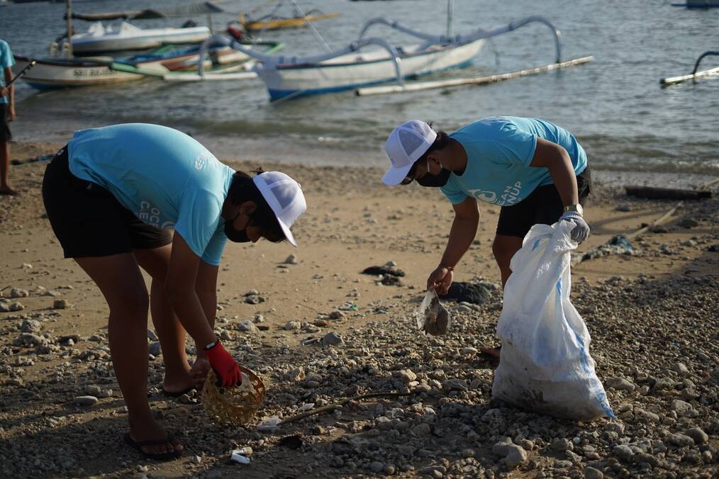 Two people cleaning up trash on a beach.
