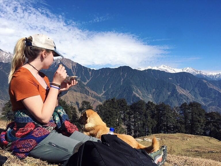 A woman sitting with a dog in the mountains.