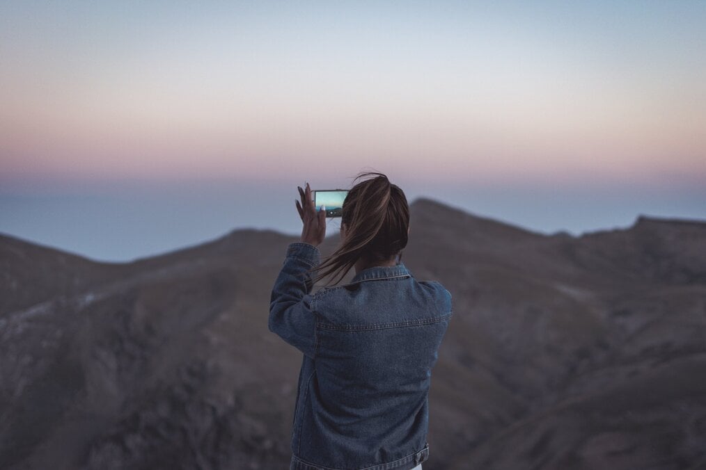 Photo by Jason Blackeye on Unsplash Woman taking a photo of a mountain.