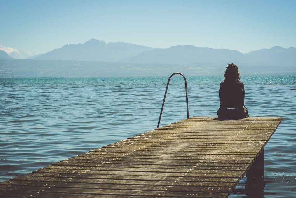 Photo by Paola Chaaya on Unsplash Woman sitting on a dock by the water.