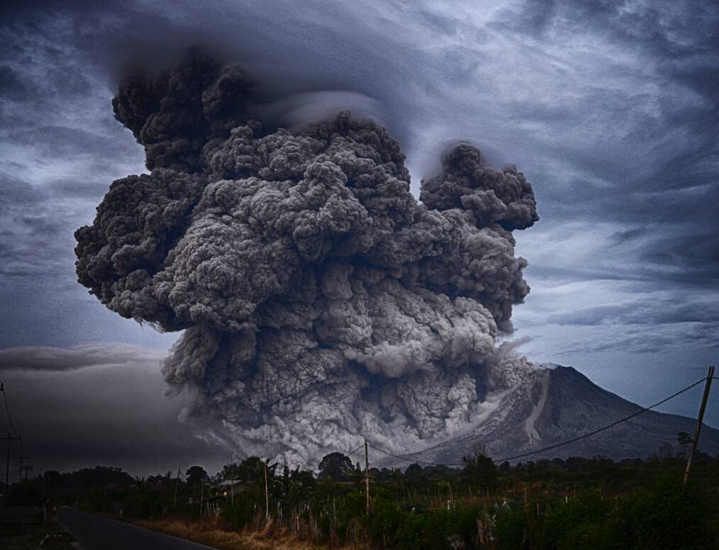 A volcano erupting with a dark cloud of smoke.