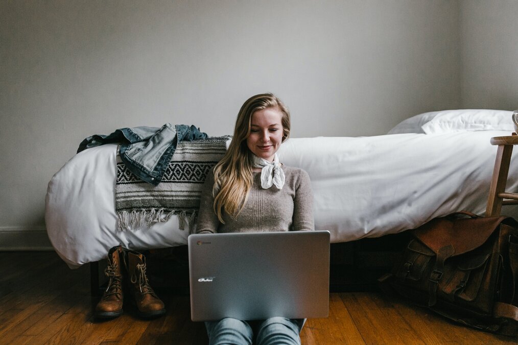 Person sitting on floor of bedroom with laptop