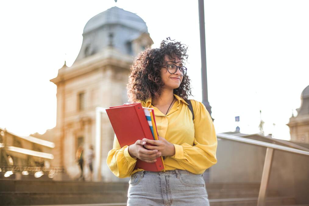 Student walking on campus with books and binder