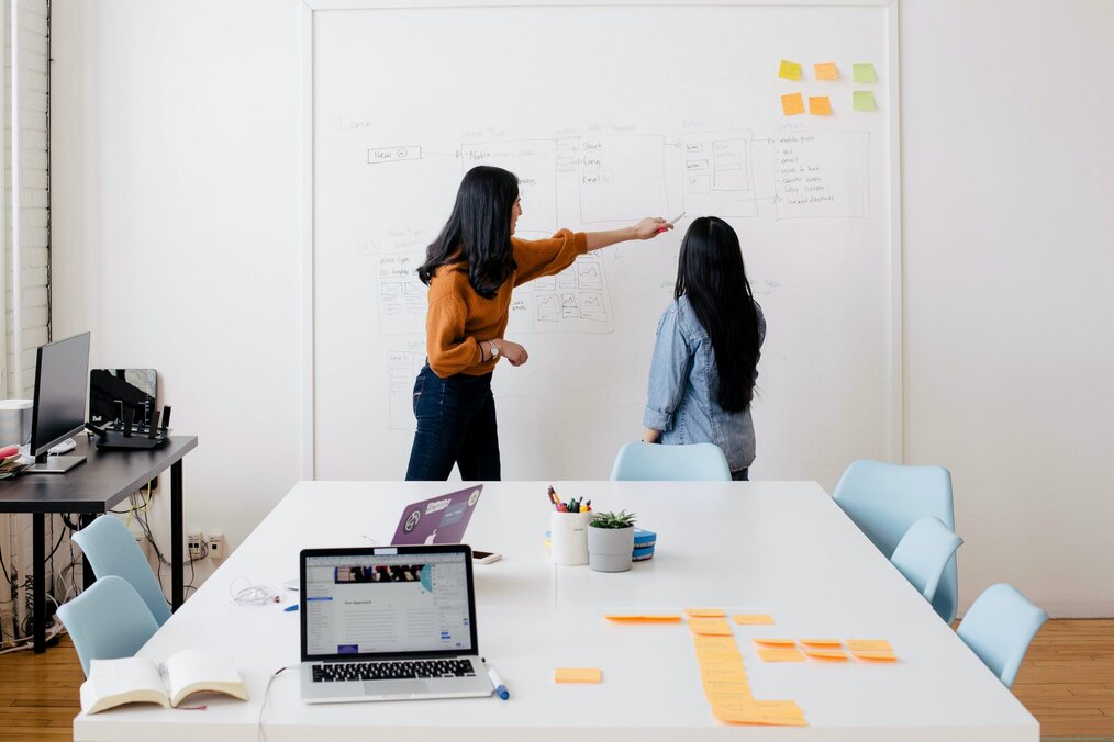 2 people in an office looking at white board and sticky notes