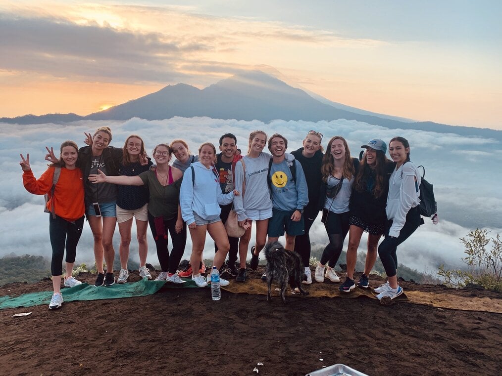 Group of travelers smiling on mountain covered with clouds as sunrises