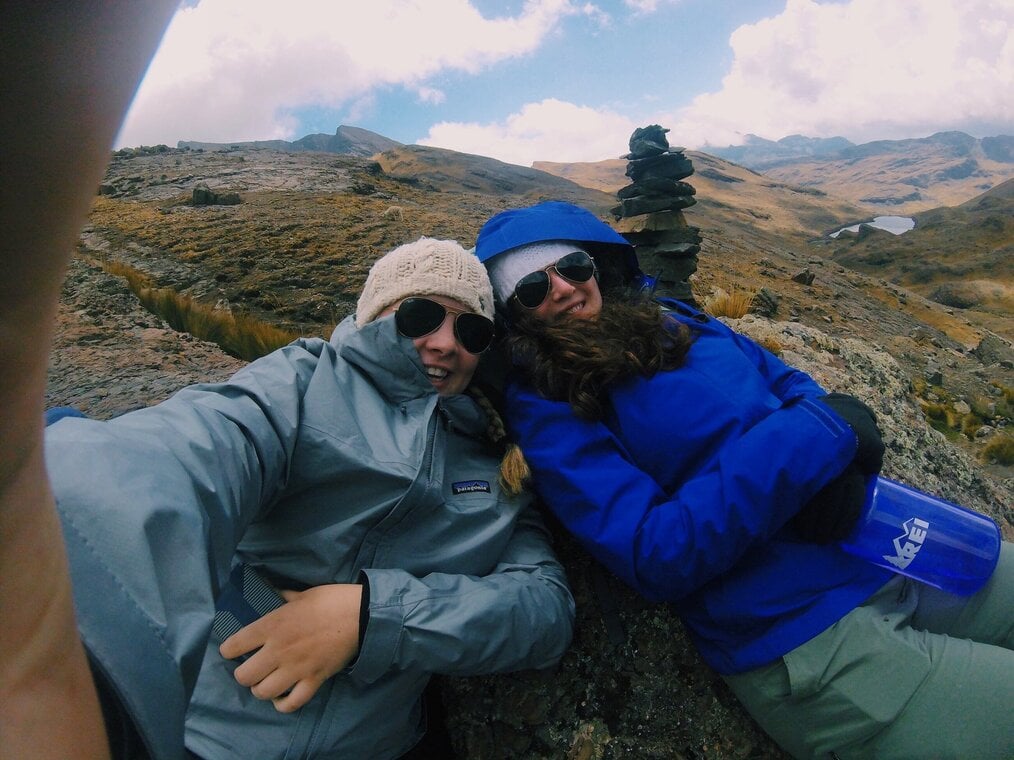 2 travelers taking a selfie while laying on a mountain