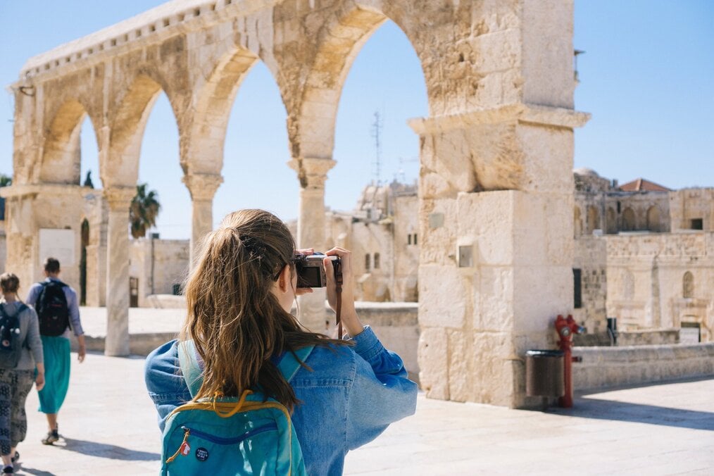 Person wearing a backpack, holding camera, and taking photos of arches