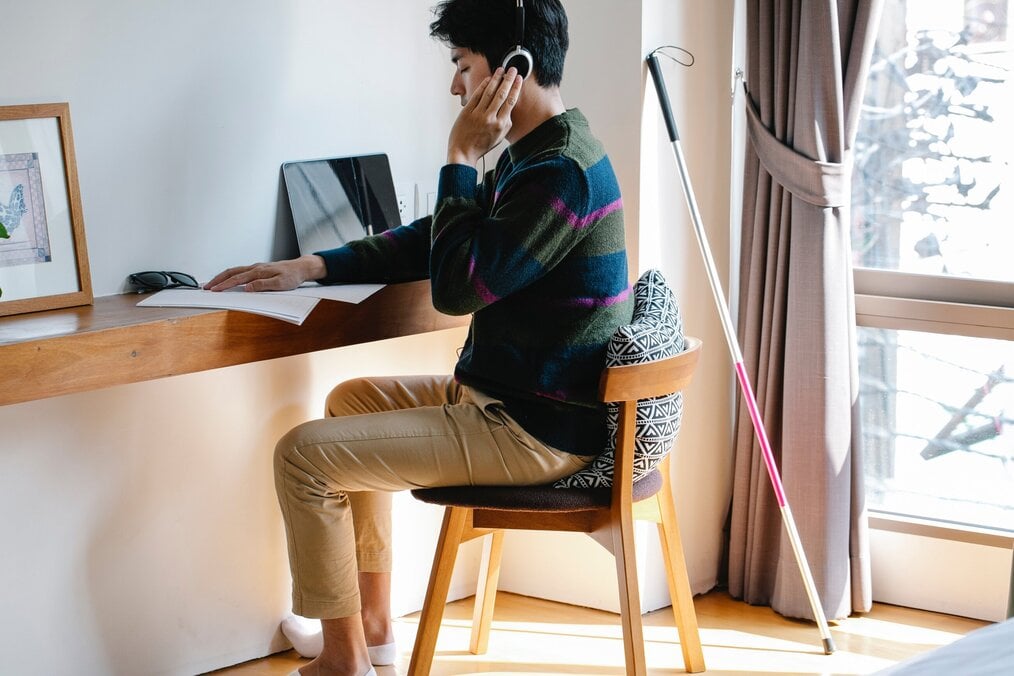 Person studying at desk wearing headphones, with a mobility cane next to them