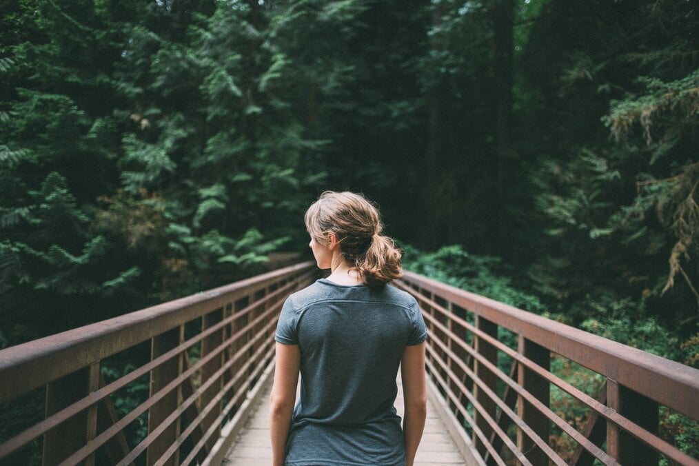 Person standing on suspension bridge in forest