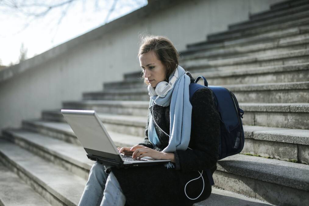 Girl sitting on stairs using laptop and wearing backpack