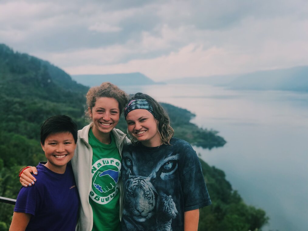 Three volunteers smiling in front of a hill and body of water