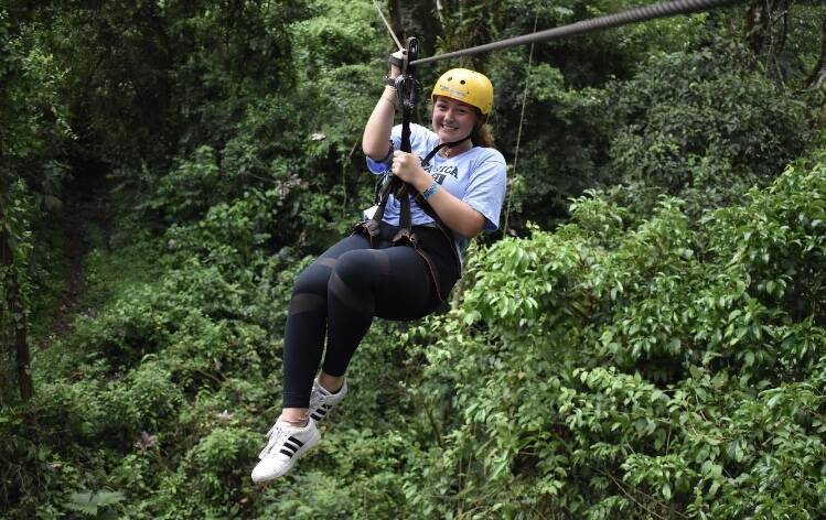 Volunteer wearing yellow helmet and ziplining through trees
