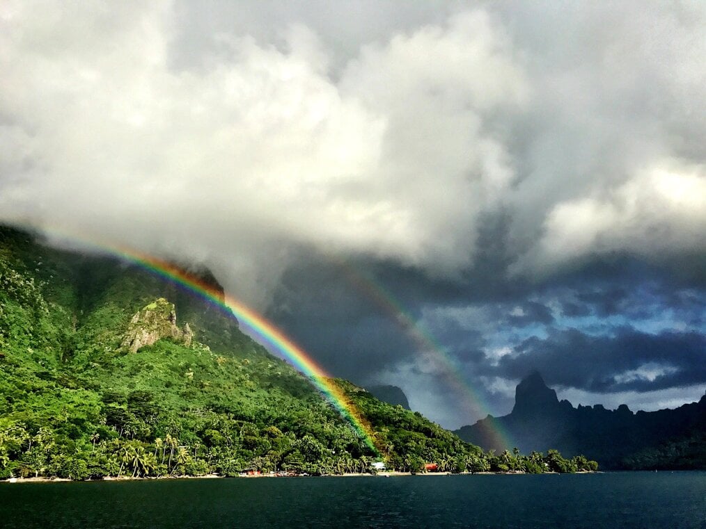 Double rainbow over a green hill and water