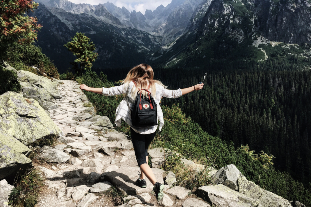 Girl hiking through mountains wearing a backpack and swinging arms