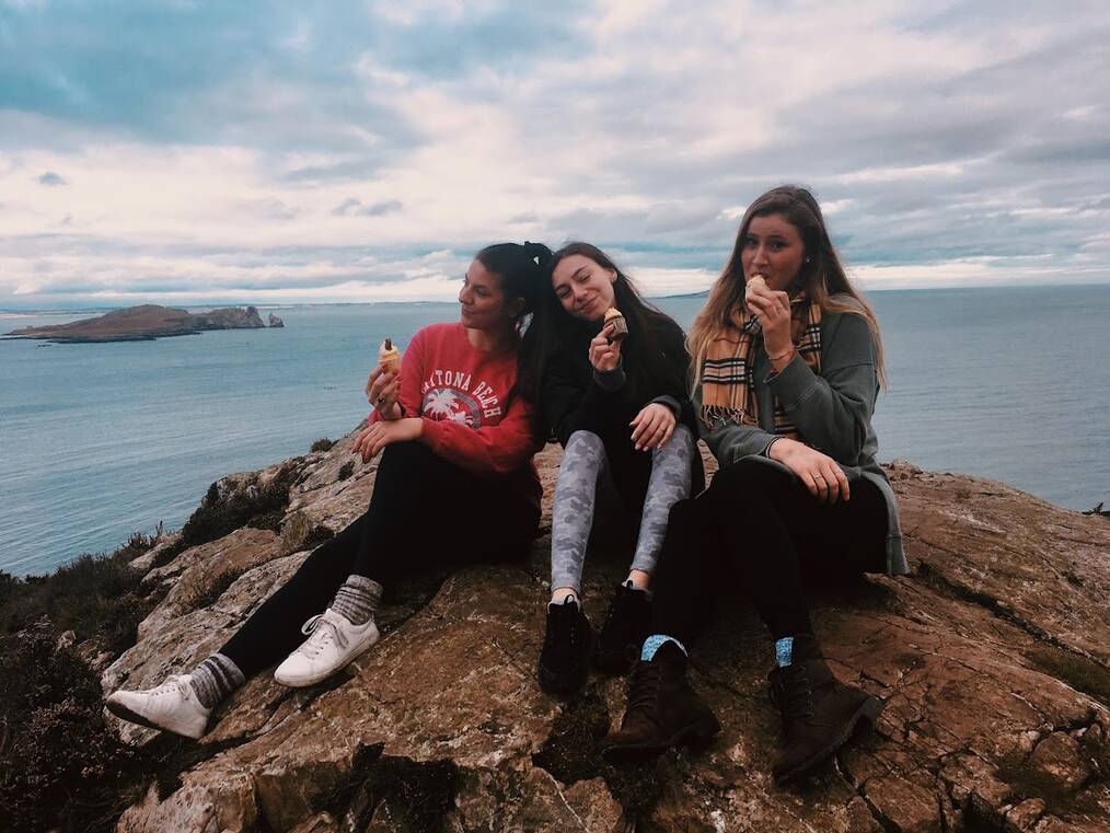 Three women sitting on a cliff in Ireland.