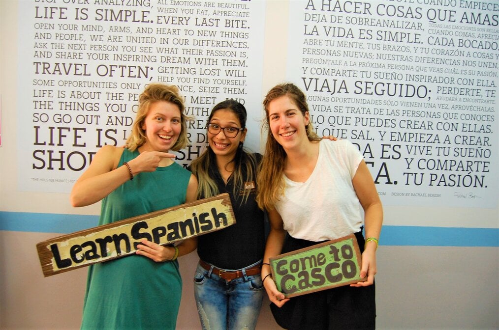 Photo by Laura Casco, Antiguo Spanish School Three girls in front of a wall holding signs to learn Spanish