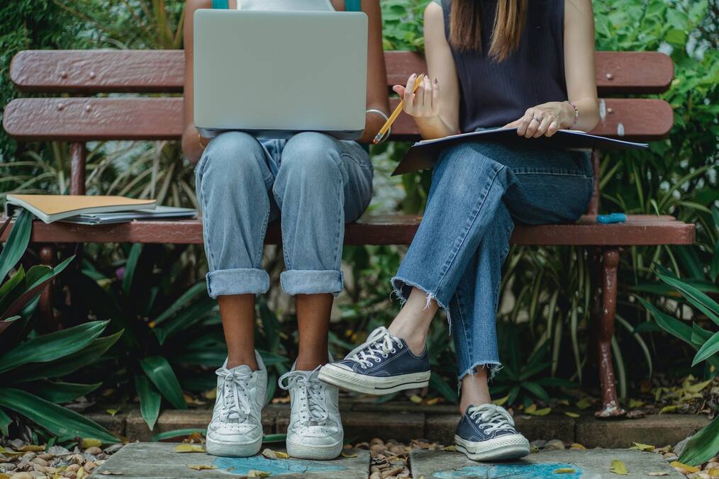2 students using a laptop while sitting on a bench