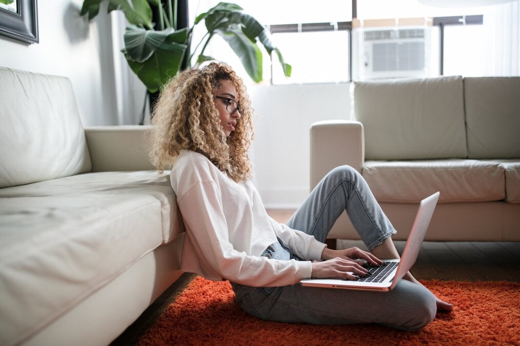 Compelling Personal Statement, Courtesy of Unsplash Woman sits on living room floor writing personal statement on laptop