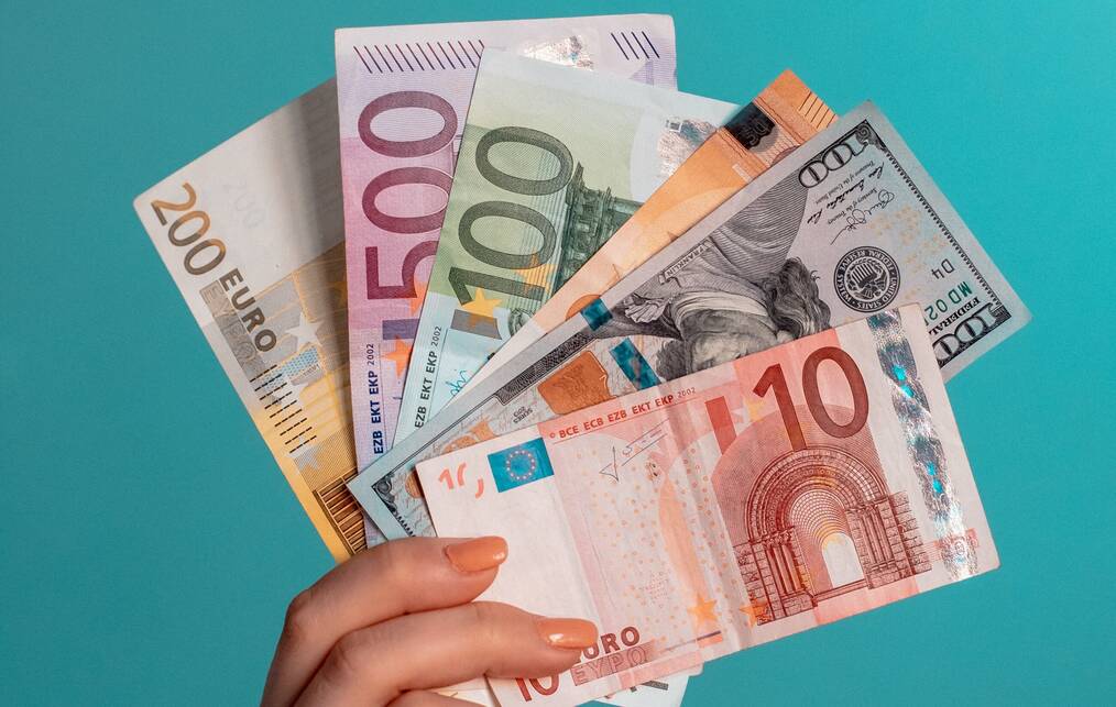 A hand holding different types of currency