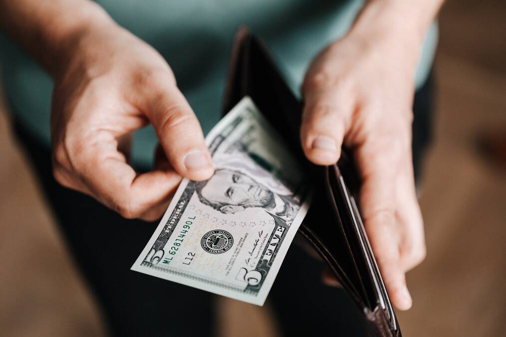 Person holding a $5 bill in wallet
