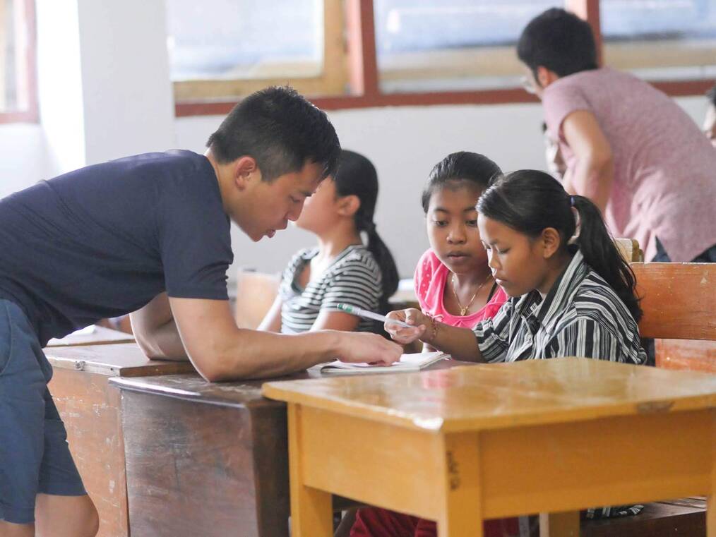 A volunteer teaching children at their desks in Bali