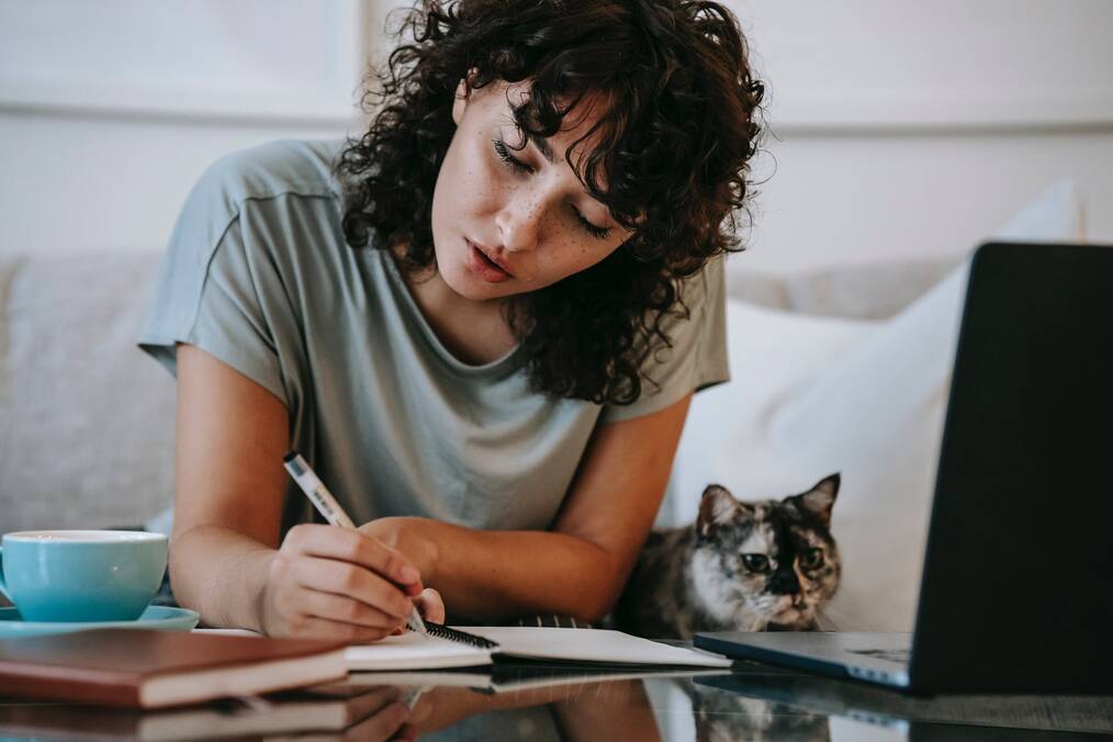A woman does homework with her cat sitting next to her