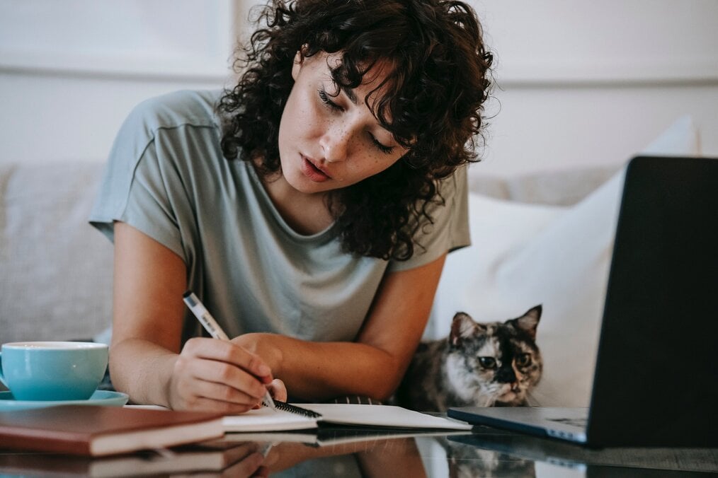 A woman does homework with her cat sitting next to her