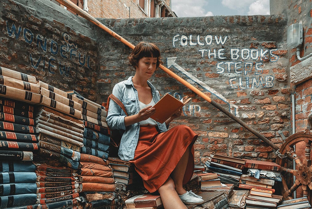 A person sitting on a staircase surrounded by books