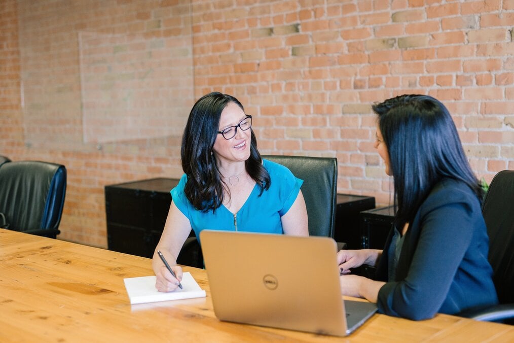 Photo by Amy Hirschi on Unsplash Two women talking in front of a laptop.