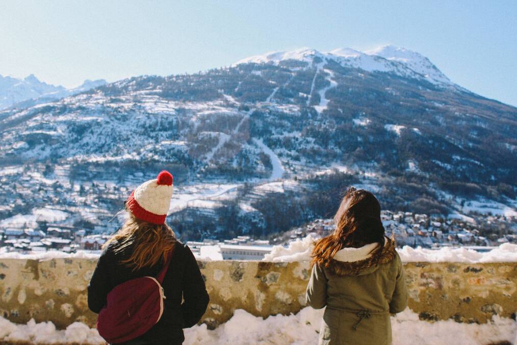Two women face away from the camera looking at a snowy hill.