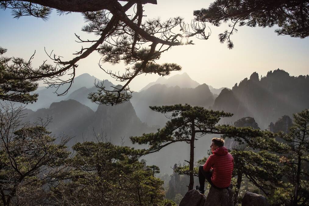 A man sitting on a rock with mountains in the background.