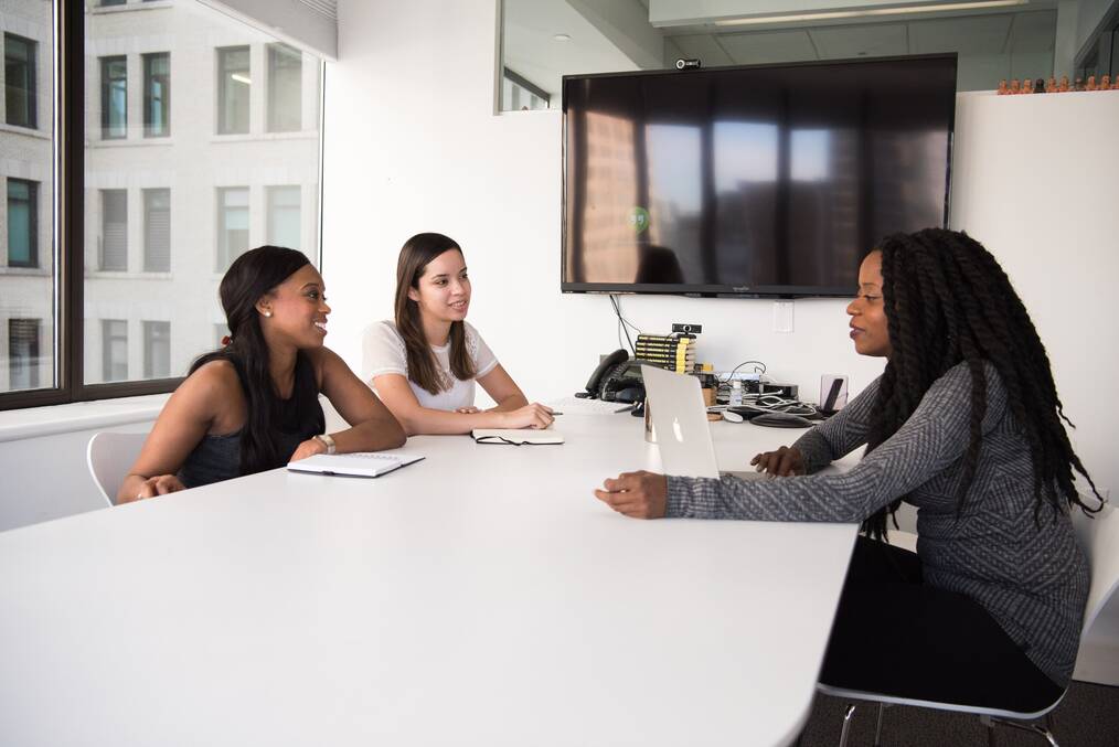 Three woman sitting around a table talking.
