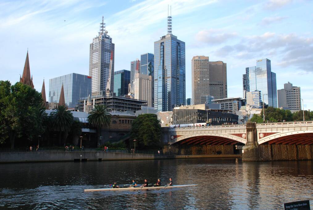 People rowing a boat on a river with the Melbourne skyline in the background.