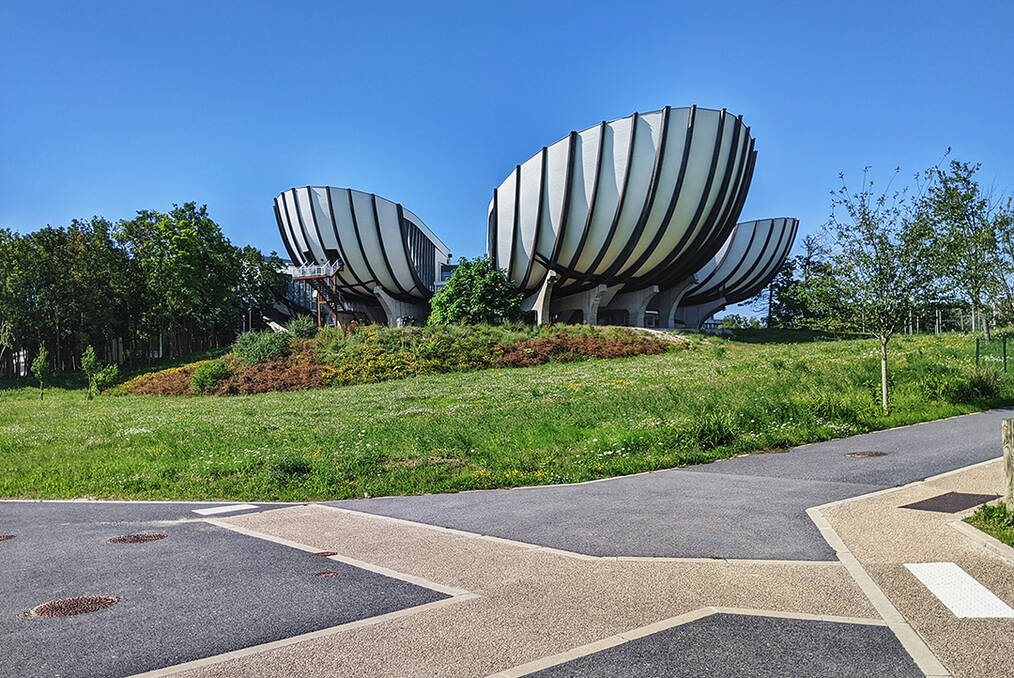 A flower shaped building behind a green patch of grass